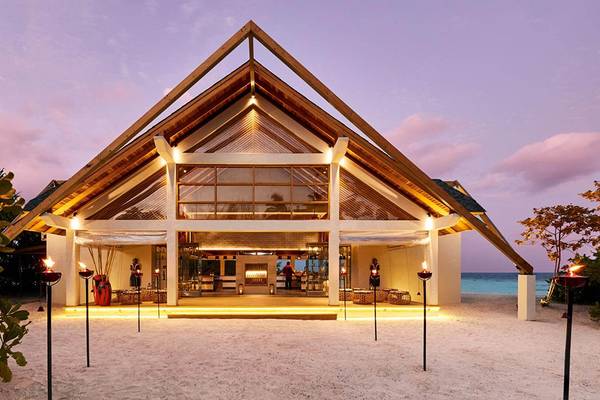 Außenansicht des Amari Havodda Maldives Hotels bei Nacht mit eingeschalteten Lichtern und Fackeln auf dem Strand.
