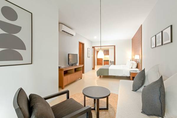 Innenansicht einer Suite im Sunprime Kamala Beach Hotel mit Bett, Fernseher, Möbeln und Klimaanlage.