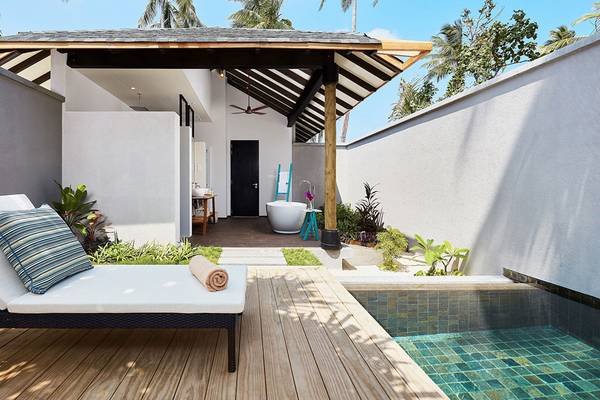 Außenbereich des Amari Havodda Maldives mit Liege, Pool und traditionellem Dach.