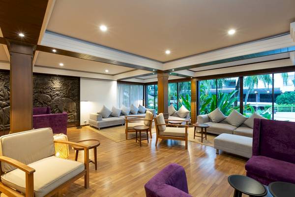 Hotellobby mit Holzboden, Sofas, Tischen und großen Fenstern mit Blick auf die Außenlandschaft.