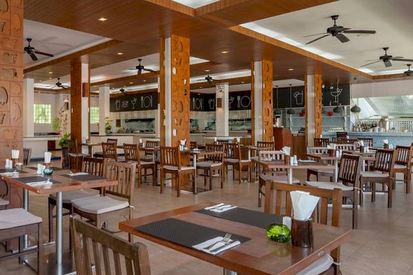Innenbereich des Sunprime Kamala Beach Restaurants mit Holztischen und Stühlen, Deckenventilatoren und einer Theke.
