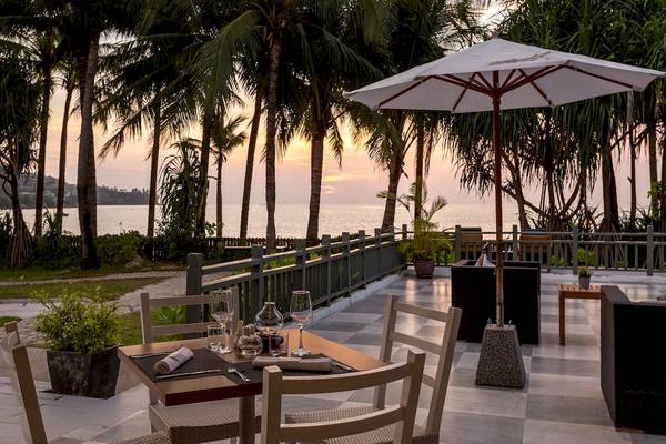 Terrasse des Sunprime Kamala Beach Hotels bei Sonnenuntergang mit Tischen, Stühlen und einem Schirm, der auf den Blick auf das Meer ausgerichtet ist.