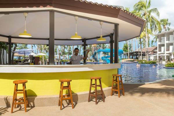 Pool-Bar im Sunwing Bangtao Beach Hotel mit gelben Stühlen und Wasserrutsche im Hintergrund.