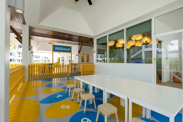 Innenbereich des Sunwing Bangtao Beach Hotels mit bunten Bodenmustern, weißen Tischen und Stühlen sowie einer Miniland-Tafel.