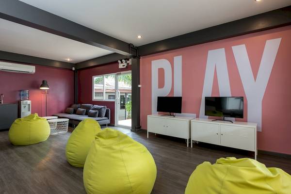 Hotelzimmer mit rosa Wand, gelben Sitzsäcken und Fernsehern, das Wort PLAY auf der Wand.