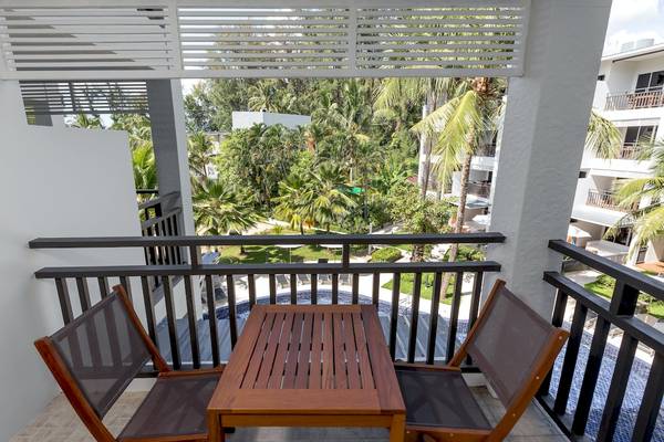 Ein Balkon des Sunwing Bangtao Beach Hotels mit einem Tisch und zwei Stühlen und Blick auf einen Swimmingpool.