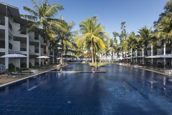 Ein großer Swimmingpool des Sunwing Bangtao Beach Hotels mit Sonnenliegen und Palmen.
