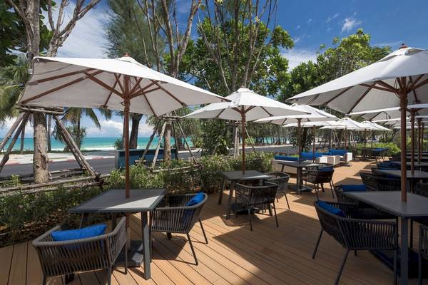 Außenterrasse des Four Points by Sheraton Phuket Patong Beach Resort mit Tischen und Stühlen unter großen weißen Sonnenschirmen.