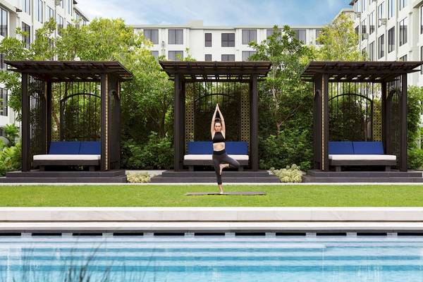 Eine Frau praktiziert Yoga auf einer Yogamatte vor einem Hotelpool.