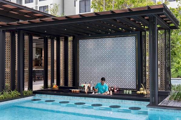 Ein Barkeeper in einem blauen Poloshirt serviert Getränke an der Poolbar des Four Points by Sheraton Phuket Patong Beach Resort.