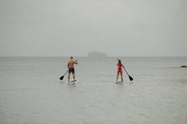 Zwei Paddler im Meer, einer in Badehose und die andere in Bikini, beide auf Paddelbrettern.