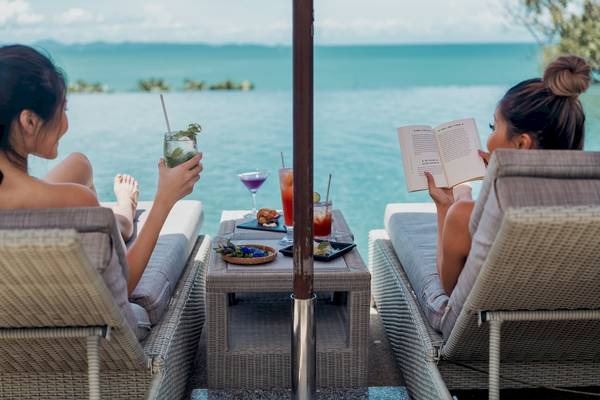 Zwei Frauen am Pool mit Getränken und einem Buch, Blick auf das Meer