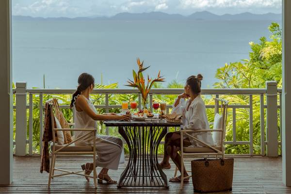 Zwei Frauen frühstücken auf der Balkonterrasse des Amatara Welleisure Resorts mit Meerblick.