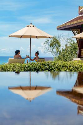 Zwei Frauen am Pool des Amatara Welleisure Resort, die Getränke genießen.