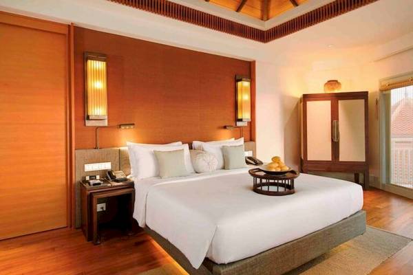 Hotelzimmer im Amatara Welleisure Resort mit großem Bett, Tisch mit Früchten und Holzmöbeln.
