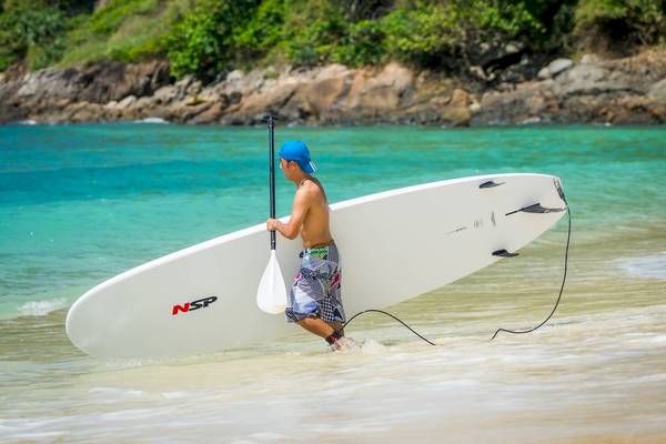 Junger Mann zieht Surfbrett im Wasser am Strand