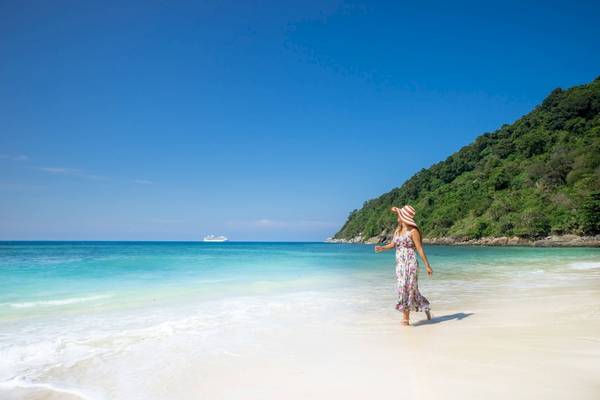 Frau am Strand des Phuket Marriott Resort & Spa Merlin Beach mit einem Kreuzfahrtschiff im Hintergrund.
