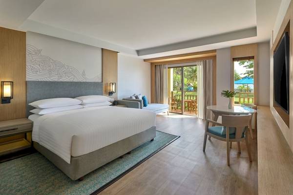 Hotelzimmer des Phuket Marriott Resort & Spa Merlin Beach mit großem Bett, Balkon und modernen Möbeln.
