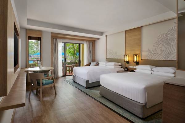 Innenansicht eines Doppelzimmers im Phuket Marriott Resort & Spa Merlin Beach mit zwei Betten, Tisch, Stühlen und Terrassenzugang.