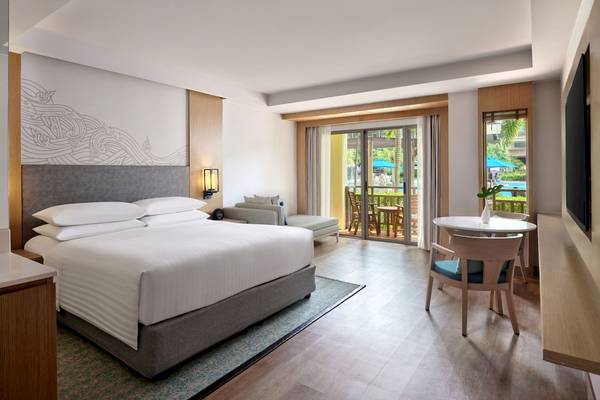 Schlafzimmer im Phuket Marriott Resort & Spa Merlin Beach mit Doppelbett, Tisch und Zugang zur Terrasse.
