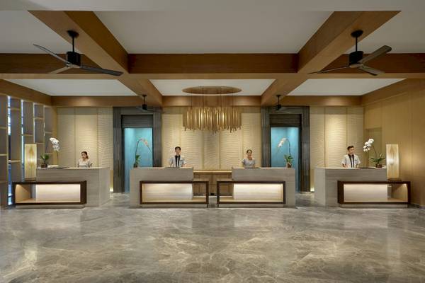Empfangsbereich des Phuket Marriott Resort & Spa Merlin Beach mit vier Rezeptionisten und einer großen Deckenleuchte.