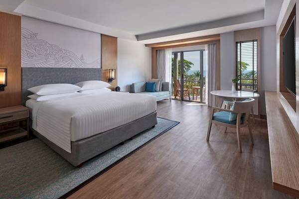 Innenansicht einer Suite im Phuket Marriott Resort & Spa Merlin Beach mit Bett, Wohnzimmer und Balkon