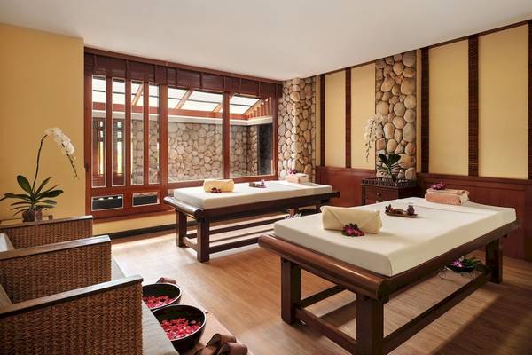 Massageraum im Phuket Marriott Resort & Spa Merlin Beach mit zwei Massageliegen, Steinwänden und Pflanzen.