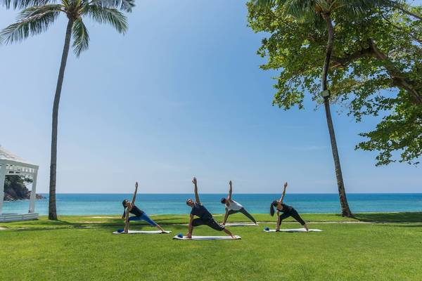 Vier Personen machen Yoga im Freien am Strand des Phuket Marriott Resort & Spa Merlin Beach.