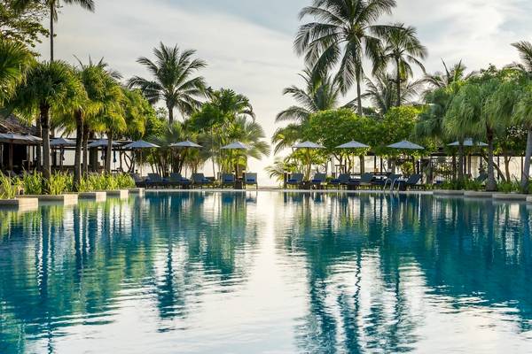 Ein großer Swimmingpool im Freien im Phuket Marriott Resort & Spa Merlin Beach mit umliegenden Sonnenliegen und Palmen.