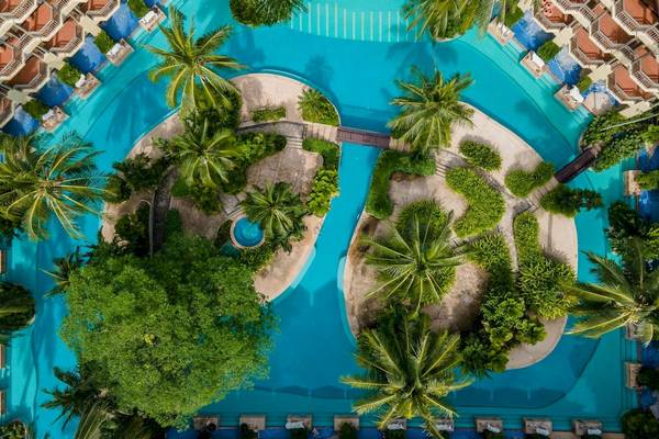 Luftaufnahme des Schwimmbads im Phuket Marriott Resort & Spa Merlin Beach mit grünen Bäumen und weißen Sonnenliegen.