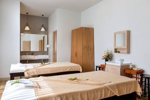 Spa-Behandlungsraum im X10 Khaolak Resort mit zwei Massagetischen, Waschbecken und Dekoblumen.