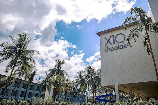 Außenansicht des X10 Khaolak Resorts mit großen Palmen und einem blauen Wasserrutsche im Vordergrund.