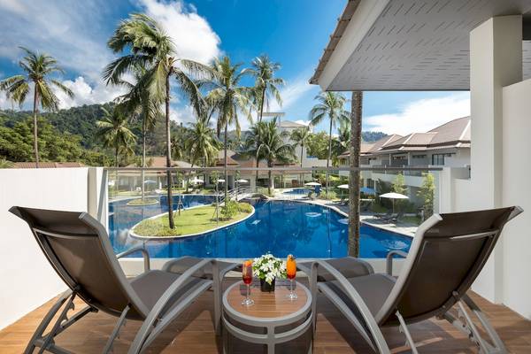 Aussicht auf den Pool vom Hotelbalkon mit zwei Liegestühlen und einem Tisch mit Getränken.