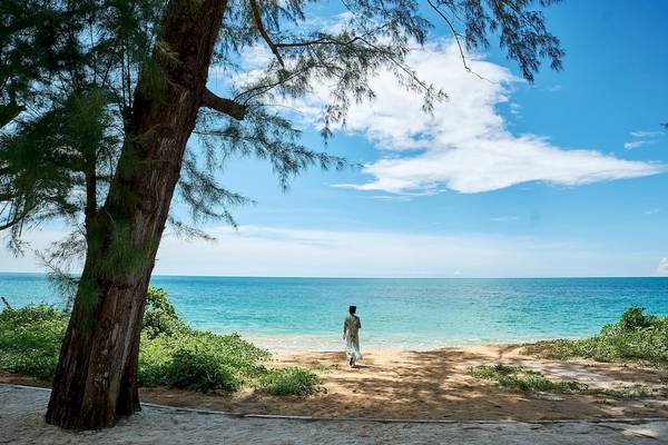 Person in einem langen Kleid steht an einem Strand des X10 Khaolak Resorts.