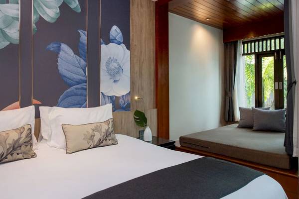 Schlafzimmer im La Flora Khao Lak Hotel mit blauen Blumentapeten, weißem Bett und grauen Kissen.