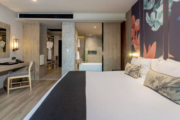 Innenansicht eines Hotelzimmers im La Flora Khao Lak, mit einem Bett, Schreibtisch und Badezimmer.