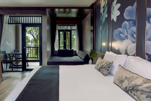 Innenansicht des Schlafzimmers im La Flora Khao Lak Hotel mit einem großen Bett, Dekor und Ausblick auf die Außenterrasse.