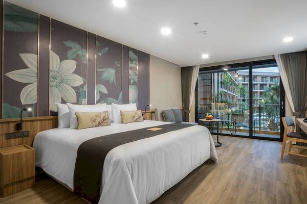 Innenansicht des La Flora Khao Lak Hotelzimmers mit Bett, Kissen, und Balkonzugang.