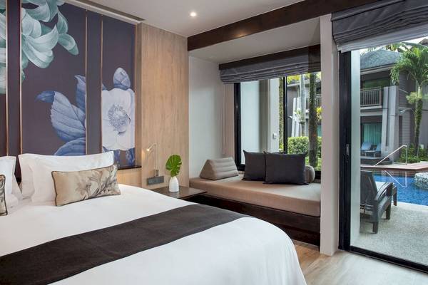 Schlafzimmer im La Flora Khao Lak Hotel mit Bett, Kissen und Pflanzendekor.