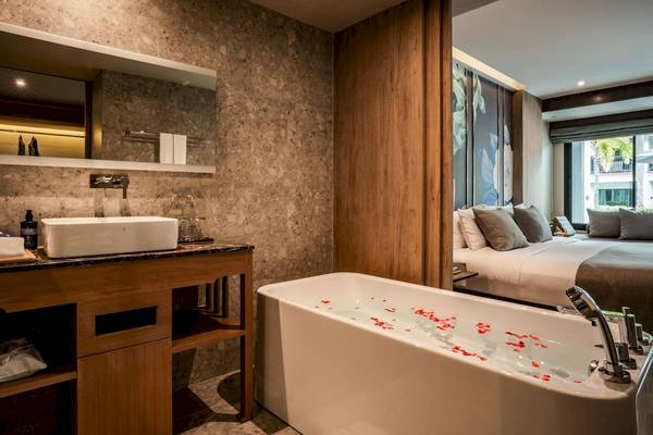 Badezimmer im La Flora Khao Lak Hotel mit Badewanne, Waschbecken und Bett im Hintergrund.