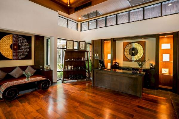 Empfangsbereich des La Flora Khao Lak Hotels mit Holzboden, Couch, Bücherregal und Schreibtisch.
