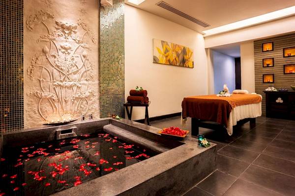 Spa-Behandlungsraum im La Flora Khao Lak mit einem großen Becken, Rosenblättern, Massagetisch und Wandverzierungen.