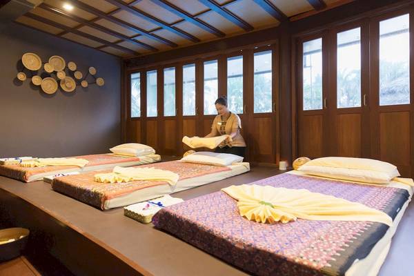 Massage-Behandlungsraum im The Haven Khao Lak Hotel mit vorbereiteten Betten und einer Frau, die ein Handtuch hält.