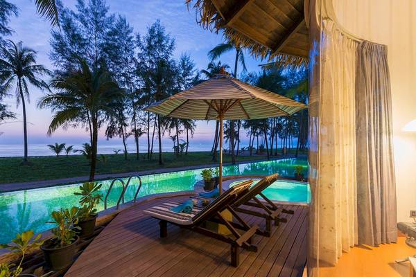 Poolbereich des The Haven Khao Lak Hotels mit Loungeliegen und einem großen Sonnenschirm.