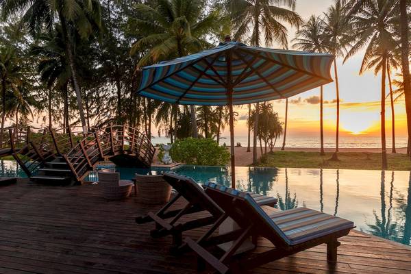 Sonnenuntergang am Pool-Lounge-Bereich des Haven Khao Lak mit blau-gestreiftem Sonnenschirm.