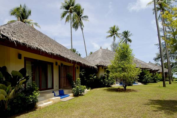 Bangsak Village Bungalows vor blauem Himmel mit Palmen und grüner Rasenfläche