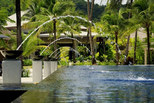 Pool mit Springbrunnen im Bangsak Village Hotel, umgeben von Palmen und Gebäuden.