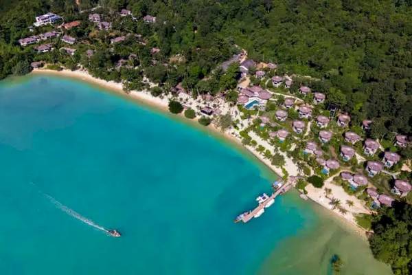Luftaufnahme von TreeHouse Villas Koh Yao mit vielen Villen am Strand und einem Boot, das anlegt.
