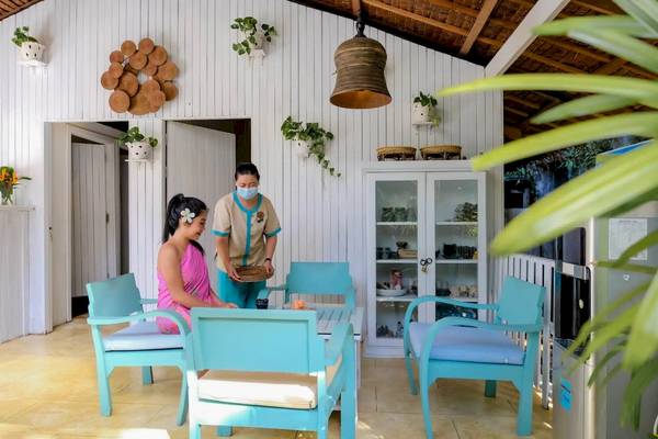 Zwei Frauen im TreeHouse Villas Koh Yao Hotel, eine sitzt auf einem Stuhl, die andere steht und serviert.