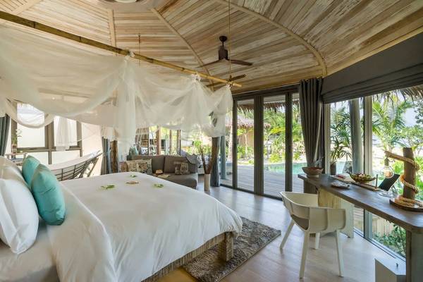 Innenansicht eines Schlafzimmers in den TreeHouse Villas Koh Yao mit einem großen Bett, einem Hängebett, einem Schreibtisch und Fenstern mit Blick auf die Natur.